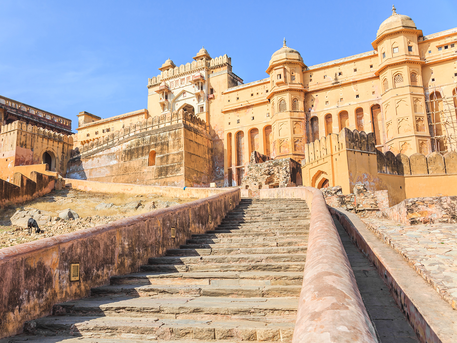 A historic sandstone fort with ornate arches and domed towers, viewed from a wide stone staircase leading up the hillside.